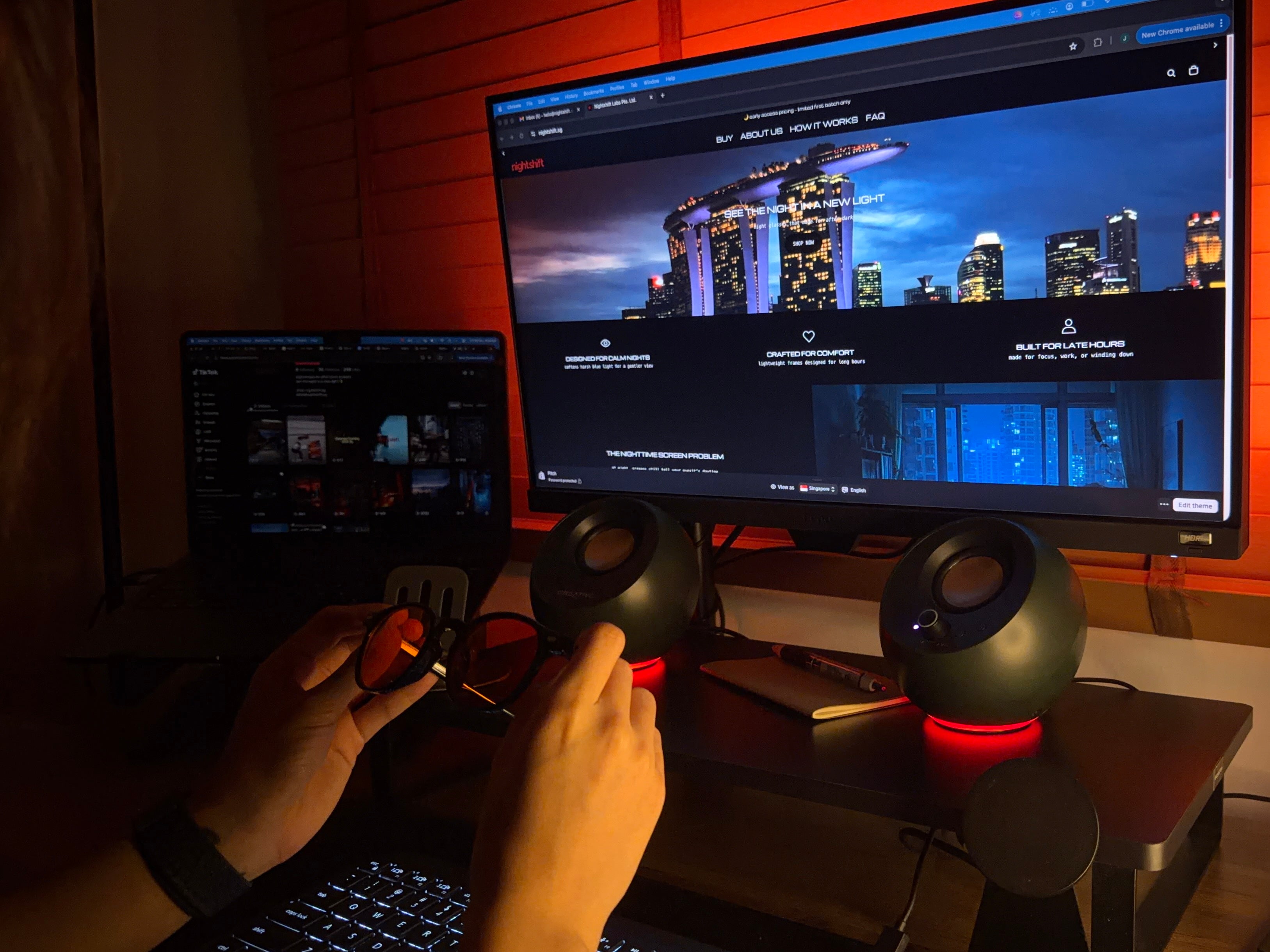 holding nightshift orange night glasses at a nighttime computer setup